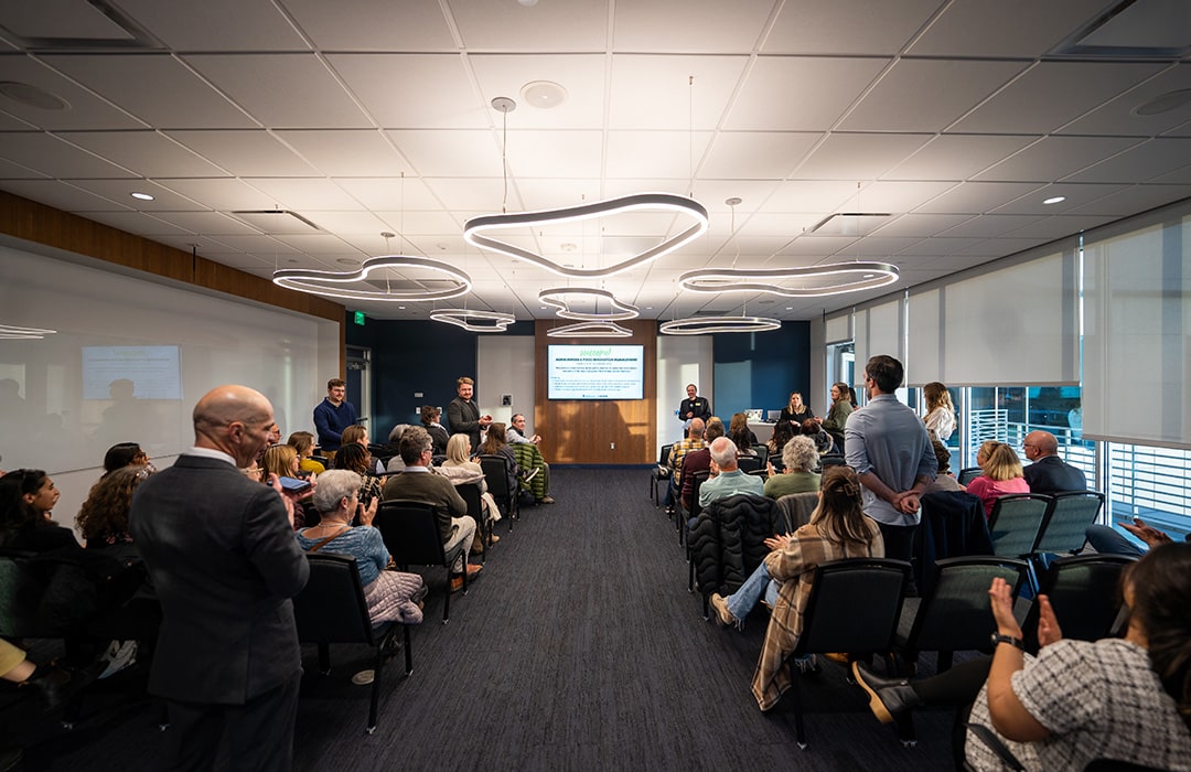 A group of people sit in a conference room and listen to a panel presentation