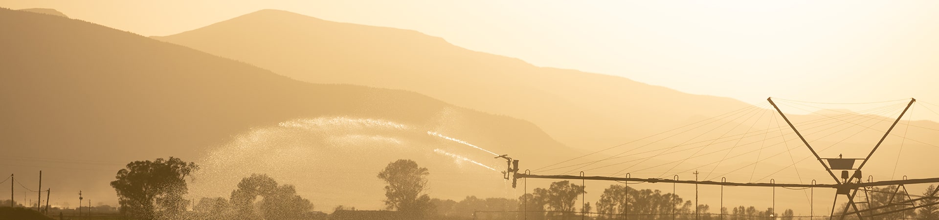A pivot sprinkler spraying water over a field at sunset